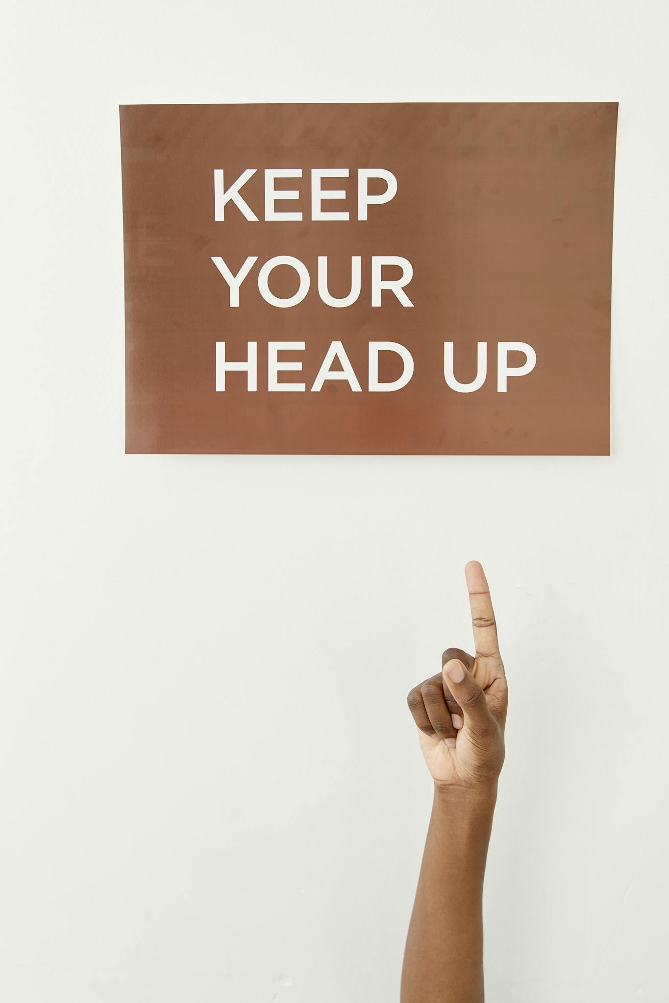 A finger points to a motivational sign reading 'Keep Your Head Up'.