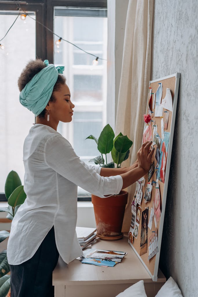 A woman working on a vision board indoors, surrounded by a cozy atmosphere and greenery.