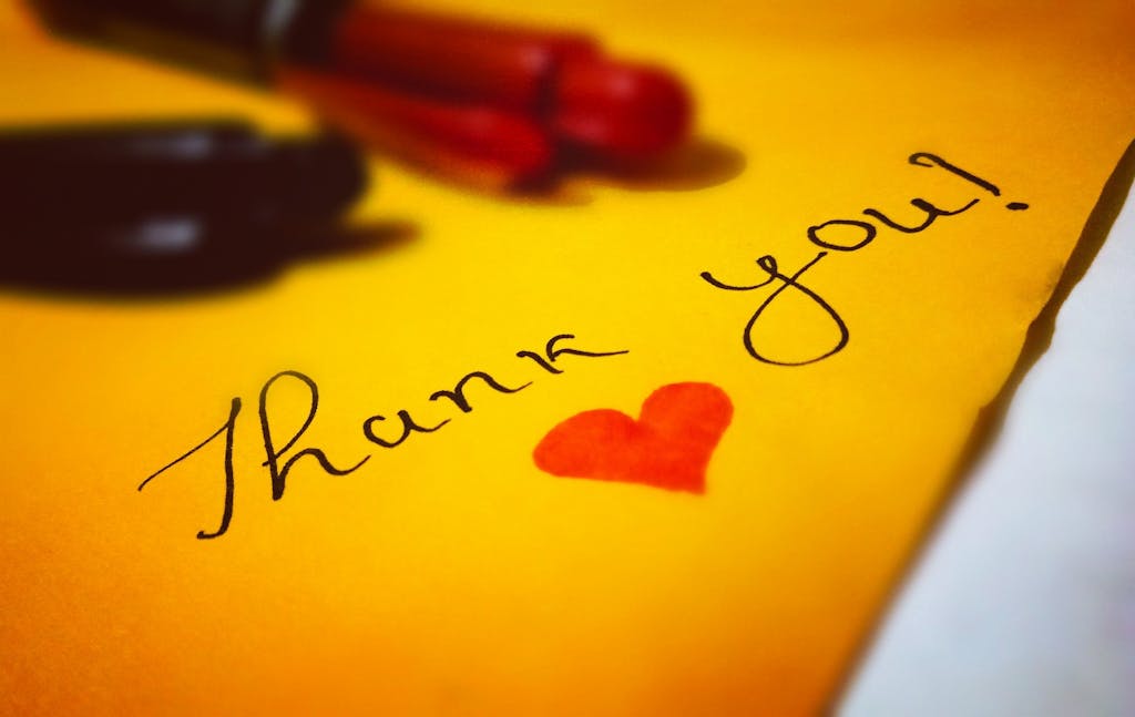 Close-up of a thank you note with a heart and pen on colored paper.