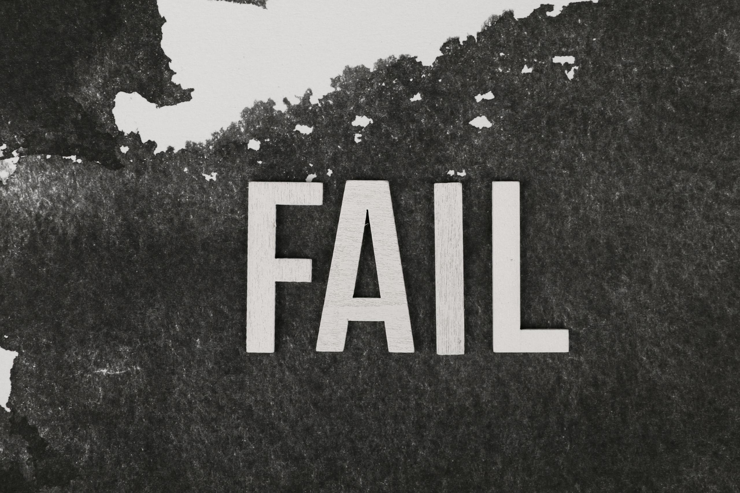 Grayscale image of the word 'FAIL' on a textured, monochrome background.
